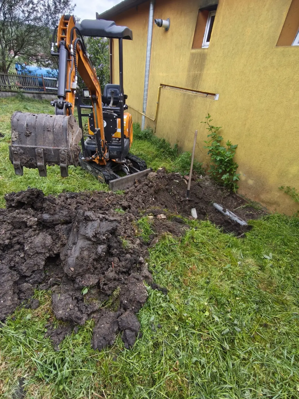 A kotró a ház fala mellett halad a nyomvonalon.